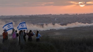 People hold Israeli flags with the Gaza strip in the distance
