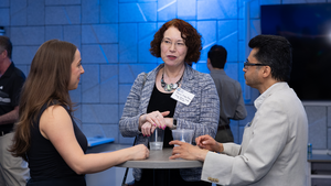 Three attendees at a Council event gather around a table with drinks and converse.