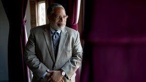 Photo of Lonnie Bunch looking out a window next to burgundy curtains