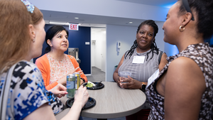 Event reception attendees standing in conversation around a table with food and drinks.