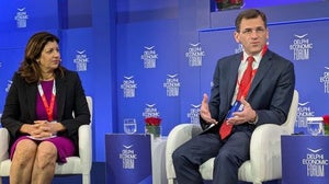Two people talk while sitting in chairs on stage
