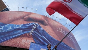 A man waves an Iranian flag under a billboard with graphic showing Strait of Hormuz and sewn lips of USPresident Donald Trump