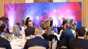 Three people sit on stage in front of an audience sitting at dinner tables