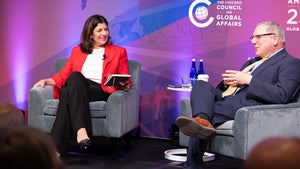 Two people sit in armchairs on stage