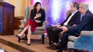 Three people sit in armchairs on stage