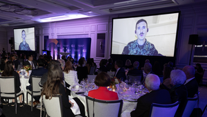 A room full of people watching someone speak on a screen