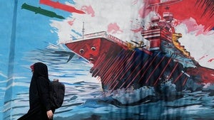 A woman walks past a mural depicting a US aircraft carrier under missile attack