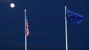 An American flag and an European Union flag fly in a night sky