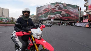 A man drives his motorbike past a huge banner showing hands firmly holding Iranian flags as a sign of patriotism, as one of them flashes the victory sign, in Tehran, Iran, Wednesday, Jan. 14, 2026. 