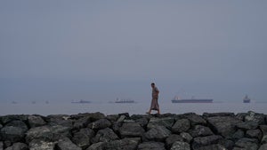 A man walks along the shore as oil tankers and cargo ships line up in the Strait of Hormuz, as seen from Khor Fakkan, United Arab Emirates, Wednesday, March 11, 2026. 